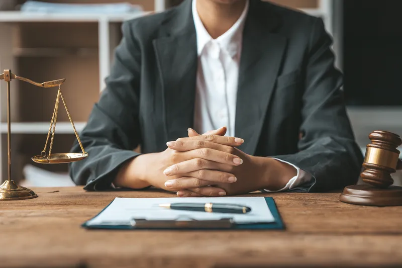 a defence lawyer in Singapore sitting with her hands together, ready to listen to her client, and a paper and pen on her desk