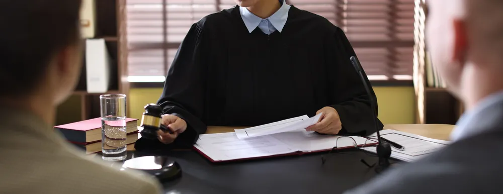 an image of a judge holding a case file in one hand and a gavel in the other with two defence lawyers in Singapore sit in front of her