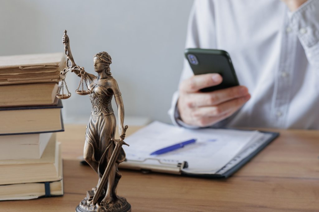 A person holding a mobile phone beside legal documents and a Lady Justice statue, reflecting legal questions about a seized phone.